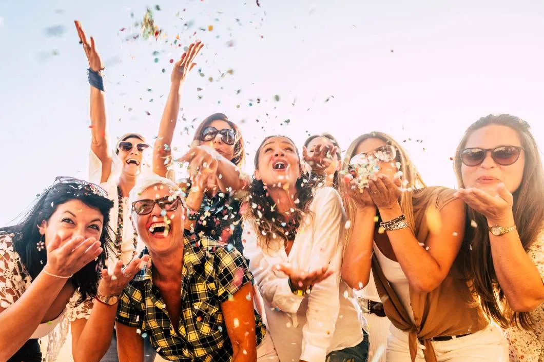 A group of friends happily gather around outside on a nice day to celebrate and throw confetti in the air.