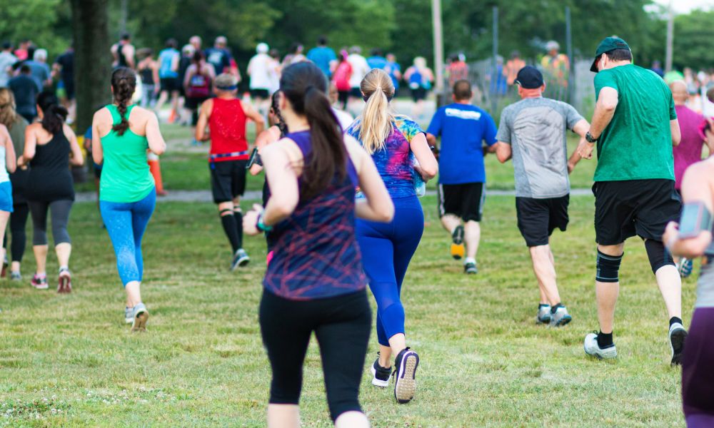 A rear view of a group of individuals participating in an outdoor run. They are running on grass in a park.