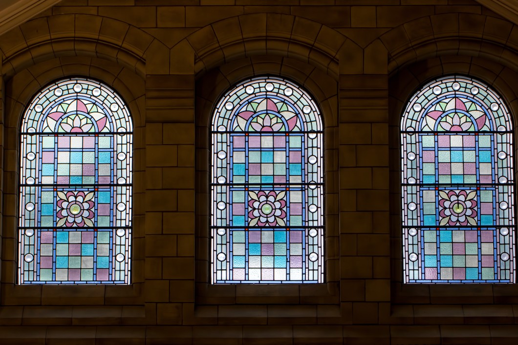 A Brief and Fascinating History of Glass Windows A trio of ornate stained-glass windows framed by an old stone building. Each window features a decorative flower.
